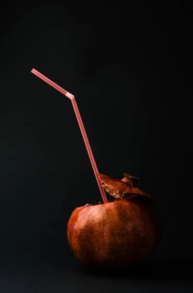 Pomegranate with a straw for drinks on a black background. Natural juice concept