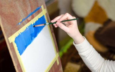 Çocuğun eli fırçayı tutuyor ve tuvale resim yapıyor, seçici odaklanma.