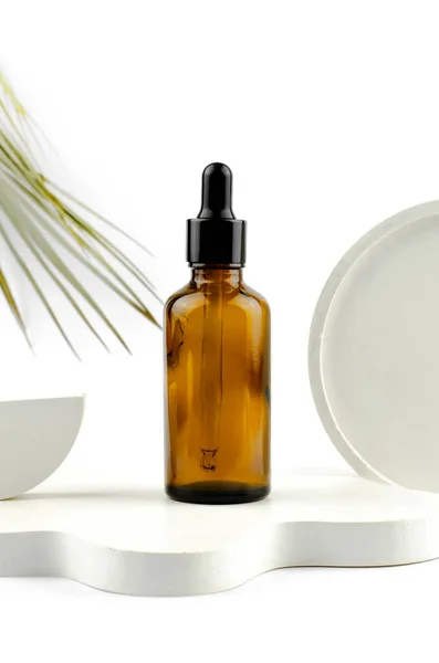 Cam şişede pipetli serum. Beyaz bir podyumda doğal ve gerekli yağ. Bir kozmetik ürün için ambalaj.