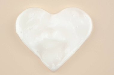 Pembe arka planda kalp şeklinde cilt kremi, yakın plan. Sağlık ve vücut bakımı teması