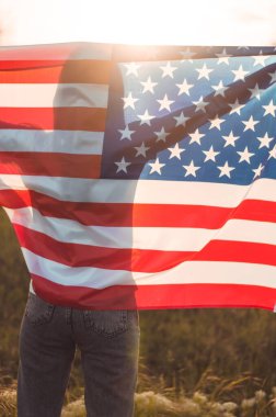 Gün batımında ABD bayrağını elinde tutan genç bir kadının arka görüntüsü. Amerika 'nın Bağımsızlık Günü. Amerikan özgürlük kavramı