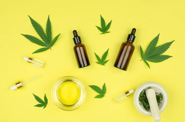 Doğal kenevir kozmetikleri. Kenevir yağlı şişeler ve kase, sarı arka planda taze kenevir yaprakları. Kozmetik CBD yağı