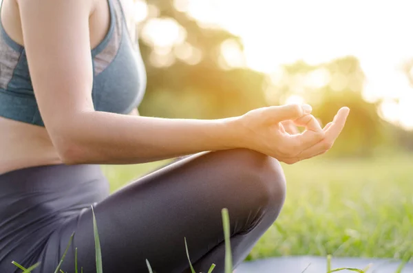 Unrecognizable woman sitting in a yoga pose. Woman meditates in the park. Unrecognizable woman practicing yoga in the park, hands close-up