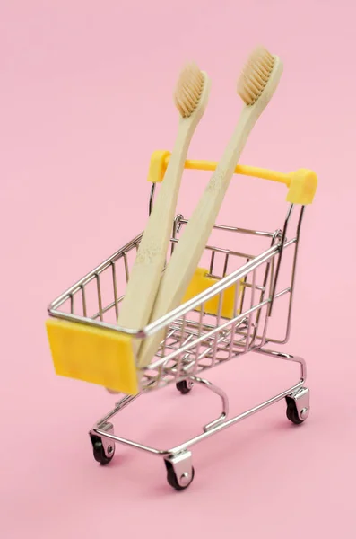 两个木制牙刷在一辆粉色背景的购物车上 个人卫生用品的环保物品 零废物 无塑料 — 图库照片