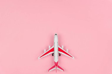 Pembe arka planda kırmızı-beyaz bir oyuncak uçağın üst görüntüsü. Seyahat kavramı