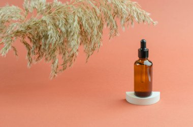 Beyaz bir podyumda bir şişe kokulu yağ. Kahverengi bir şişede damlatan yağ ya da serum. Kozmetik, vücut bakımı.