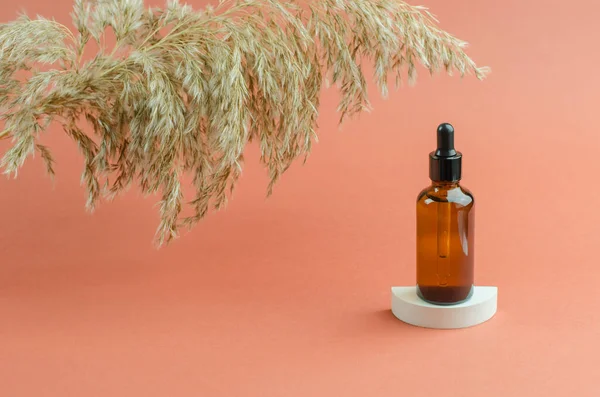 Beyaz bir podyumda bir şişe kokulu yağ. Kahverengi bir şişede damlatan yağ ya da serum. Kozmetik, vücut bakımı.