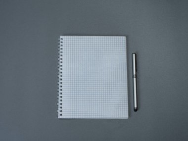 Kafeste bir çalışma kitabı ve gri arka planda bir kalem.
