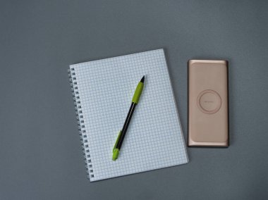 Kafeste bir çalışma kitabı, bir kalem bir kalem ve gri arka planda kablosuz güç bankası.
