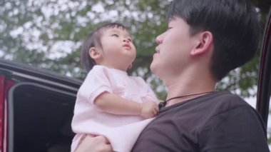 Asyalı, genç bir baba kucağında sevimli bir kız çocuğu, ağaçların altındaki aracın yanında duran küçük çocuk, aile üyesi mutluluk bağı, çocukluk öğrenme yeteneği, çocukluk merakı, ebeveynlik ve sorumluluk.