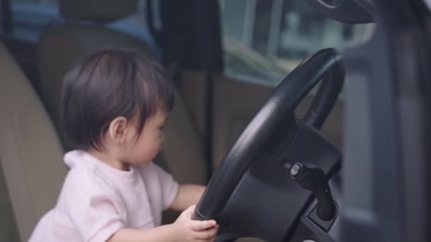 運転席に座っている車のステアリングホイールで遊ぶアジアの女の子 子供の好奇心と純粋さ 幸せな子供の学習スキル経験 車の中で無邪気な幼児年齢女性 子供の頃の学習能力 夢の仕事 — ストック動画