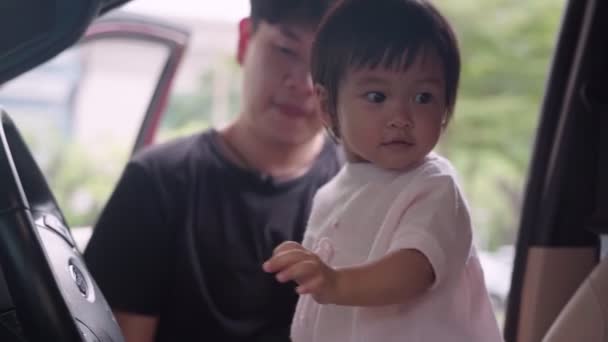 アジアの若い大人の父親は車の中の運転席に彼の赤ちゃんの女の子を再生します 家族旅行に運転するふりをステアリングホイールで遊んで赤ちゃん 家族幸福結合 子供の頃の学習能力 無実と好奇心 — ストック動画