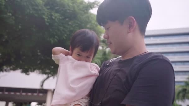 家族が公園の中に集まって アジアの若い父親が彼の腕に赤ん坊の少女を抱き 家族の暖かさが公園で一緒に時間を過ごし 幼児期の発達 愛のケア — ストック動画
