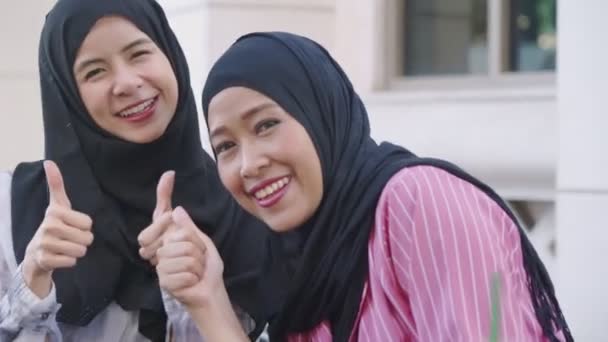 两名亚洲穆斯林女性在下午的咖啡休息时间佩戴头巾 向她的朋友展示智能手机屏幕 坐在咖啡店外面 在网上张贴照片 朋友团聚快乐 无线网络连接 现代宗教生活 — 图库视频影像