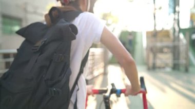 Genç bir kızın gündelik giyinmiş, bisikletini şehir üst geçidine iterken, iş yerine bisikletle giderken, maliyetten tasarruf ederken, çevreyi korurken ya da masraftan kurtulurken yakın plan çekimleri.