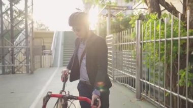 Genç Asyalı mutlu iş adamı kasklarıyla bisiklet sürerken akşam şehir yeşili parkında güzel bir yaz havası ve arka plan olarak güneş ışığının yansıması, sağlıklı şehir yaşam tarzı kavramları, çevresel koruma ya da sorunlar, yeşil enerji