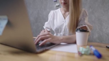 Asyalı sarışın ofis çalışanı dizüstü bilgisayarı kullanarak yüksek lisans tez projesi için bilgi topluyor, öğrenmek için dizüstü bilgisayar kullanıyor, klavyede, ev ofisinde daktilo kullanıyor, kablosuz internet bağlantısı, kazançlı beceriler