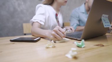 Genç sarışın işçi dizüstü bilgisayara bakıyor, önemli notlar alıyor, online konferans sonrası, buruşuk kağıtlar problem yaratıyor, yanlış yazma, başarısızlığa tepki veriyor, başarısız fikirleri çöpe atıyor, modern teknoloji ve günlük yaşam, evden çalışma.
