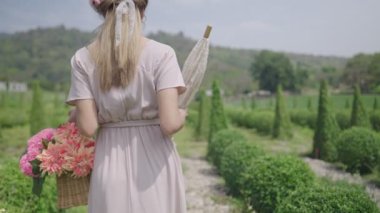 Genç, zarif, güzel bir kız, klasik bir Avrupa dekoru bahçesinde yürüyor, doğal yaz güneşi arka planda parlıyor, tatilde tatil macerasından zevk alıyor, POV takipçisi, sürdürülebilir yaşam tarzı, farklı tipte eko