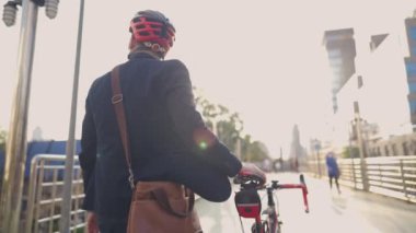 İş adamı kafasında kaskla resmi kıyafetler giyip trafiğin en yoğun olduğu saatte bisikletini üst geçitten geçiriyor. Genç profesyonel, trafikten uzak, çevresel koruma veya sorunlardan uzak, kentteki bir caddeye bakmaktan keyif alıyor, harcamalardan tasarruf ediyor