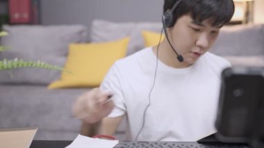 Asyalı genç anne çalışanı kulaklık takıyor müşteri bilgilerinden notlar alıyor, mikrofon ile ses bağlantısı kuruyor, personelle canlı görüşme, sosyal mesafeler, evde çalışma, kazançlı beceri, ikinci iş ve gelir