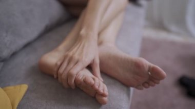 Yakın plan kadın el masajı, gri kanepeye uzanmış model evde dinlenmeye çalış, ayak masajı, kas ağrısı, yalınayak hafif deri, baldır kaslarına kramp, kas masajı, kas stresi.