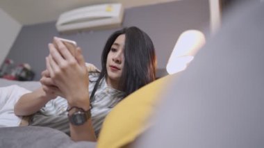 Genç Asyalı kadın rahat kanepeye uzanmış akıllı telefon kullanıyor, online alışveriş, kablosuz internet bağlantısı, kablosuz internet teknolojisi ve modern yaşam tarzı, çevrimiçi kendi kendine öğrenme konsepti, hafta sonu aktivitesi, bilgi ve becerilerin geliştirilmesi.