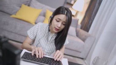 Çağrı merkezi operatörü olarak evden iş yapan güzel bir Asyalı kadın, çevrimiçi ağ bağlantısı, kulaklık takan bir kadın, müşterilerle konferans görüşmesi internet üzerinden iş alımı, ev içi oturma odası, ev içi