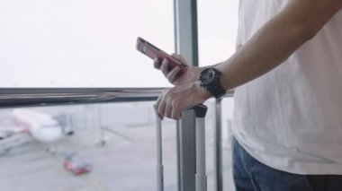 Genç erkek havaalanı terminalinin içinde akıllı telefon, havayolu seyahati, valiz çantası, bilet rezervasyonu, göçmen bürosuna taşınma. 