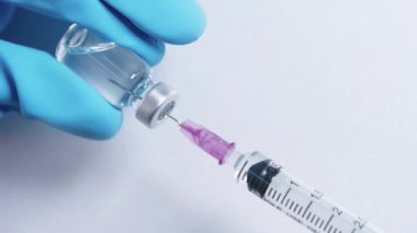 Mavi koruyucu eldivenler şırınga enjeksiyonu şişeden Covid-19 aşısını, ilaç iğnesini steril şırınga şişelerini, biyoteknoloji bağışıklığını, beyaz arka planı emer.