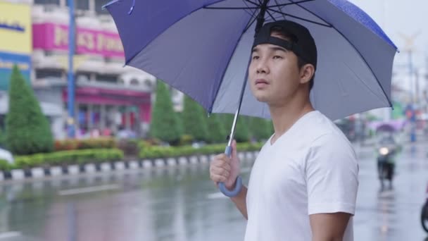 Junger Asiatischer Mann Mit Blauem Regenschirm Der Auf Dem Bürgersteig — Stockvideo
