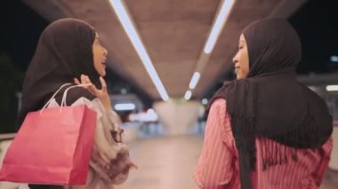 İki Asyalı Müslüman kadın alışverişe çıkıyor, arkadaşlar işten sonra bir araya geliyor, maaşlı işçi para harcıyor, arkadaşlar metropoliten yürüyüş yolunda yürüyor, alışveriş torbasını tutuyor, satış terfisi, kadınlık cemiyeti, hafta sonu dinlendirici aktiviteler.