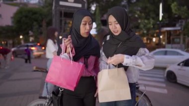 İki Asyalı Müslüman kadın alışverişe çıkıyor, arkadaşlar işten sonra bir araya geliyor, maaşlı işçi para harcıyor, arkadaşlar metropoliten yürüyüş yolunda yürüyor, alışveriş torbasını tutuyor, satış terfisi, kadınlık cemiyeti, hafta sonu dinlendirici aktiviteler.