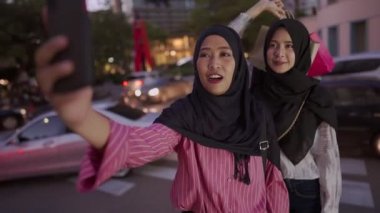 Çok ırklı Müslüman iki kız arkadaşın yüz ifadeleri takınarak, selfie çekerek, akıllı telefon kullanarak şehir merkezinde takılarak, sosyal medyada alışveriş malzemelerini göstererek, modern insanların iyi ilişkilerden, hobilerinden,