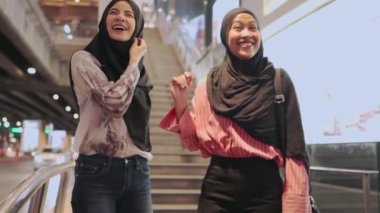 İki Asyalı Müslüman kadın alışverişe çıkıyor, arkadaşlar işten sonra bir araya geliyor, maaşlı işçi para harcıyor, arkadaşlar metropoliten yürüyüş yolunda yürüyor, alışveriş torbasını tutuyor, satış terfisi, kadınlık cemiyeti, hafta sonu dinlendirici aktiviteler.