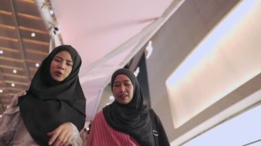 Düşük açılı çekim, çok ırklı Müslüman kadınlar alışveriş merkezinin merdivenlerinden aşağı iniyor, alışveriş günü, arkadaşlar birlikte eğleniyorlar, kağıt torbanın içine bakıp sohbet ediyorlar, mutluluk için para harcıyorlar, modern insanlar iyi bir ilişkiden hoşlanıyor, hobi olarak.