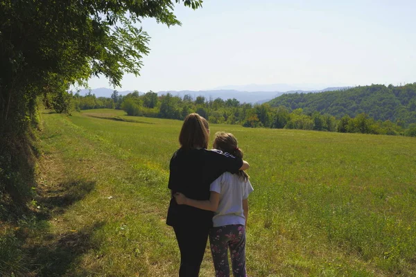 İki kız kardeş bir çayırda birbirlerine sarılırlar.