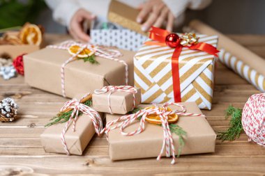 Noel hediyesini paketleyen kadınların elleri, kapatın. Ahşap zemin üzerinde dekoratif öğeler ve malzemelerle hazırlıksız hediyeler, üst görünüm. Noel ya da Yeni Yıl Kutlama Konsepti. Adım adım.