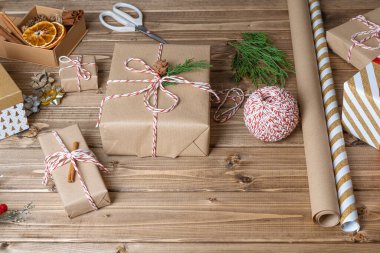 Noel hediyesini paketleyen kadınların elleri, kapatın. Ahşap zemin üzerinde dekoratif öğeler ve malzemelerle hazırlıksız hediyeler, üst görünüm. Noel ya da Yeni Yıl Kutlama Konsepti. Adım adım..