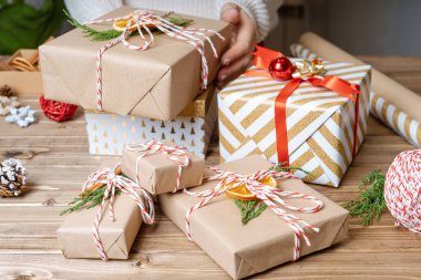 Noel hediyesini paketleyen kadınların elleri, kapatın. Ahşap zemin üzerinde dekoratif öğeler ve malzemelerle hazırlıksız hediyeler, üst görünüm. Noel ya da Yeni Yıl Kutlama Konsepti. Adım adım.