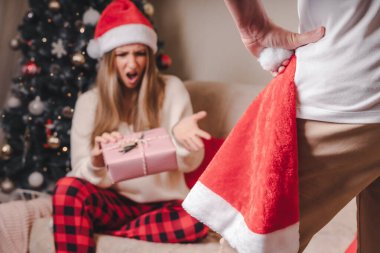 Arka planda, Noel Baba şapkalı kızgın adam ve Noel ağacının yanında hediye kutusu olan mutsuz genç kadın var. Çift sorunlu kavram.