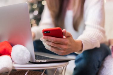 Cep telefonu ve dizüstü bilgisayarı olan kadın ellerini kapat, Noel tatillerinde ev ofisinden uyanan serbest çalışan kız ve online alışveriş. Uzaklık öğrenimi, çevrimiçi eğitim ve çalışma.