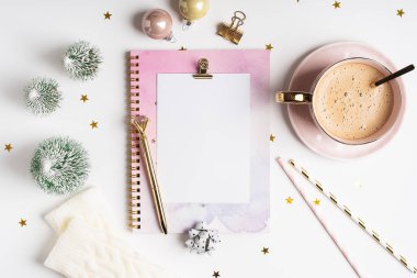 Masaüstü boş planlayıcı. Beyaz çalışma masasının arka planında bir fincan kahve ve Noel süslemesi. Üst manzara topları, köknar ağacı, ataçlar, tebrik kartı, el işi defterleri ve kalem..