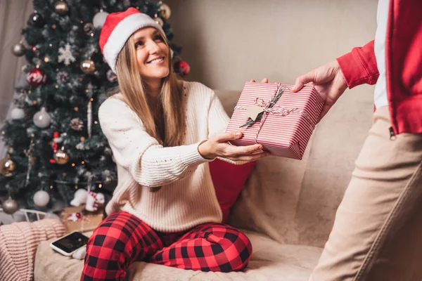 Vista trasera de cerca del hombre en suéter rojo sosteniendo una caja de regalo de Navidad a sus espaldas mientras está de pie cerca del árbol de Navidad decorado. — Foto de Stock