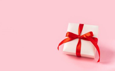 Pembe arka planda kırmızı yay ve kalp olan hediye ya da hediye kutusu