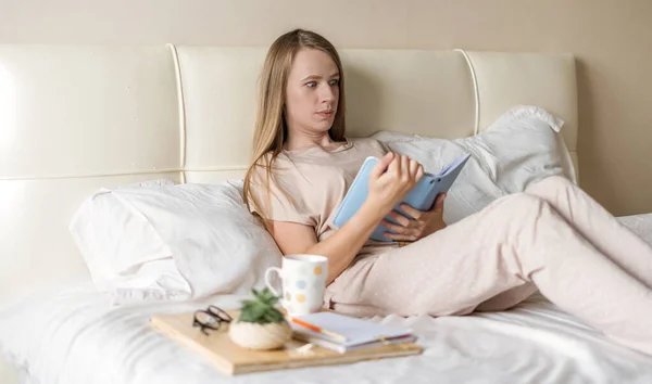 Surprised woman in bed reading with notepad