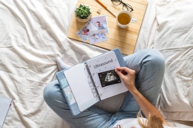 Kırpılmış kadın elleri kahveyi tutuyor ve aile fotoğrafı albümü izliyor. Anne yatağa otur ve küçük oğlunla albüm izle.