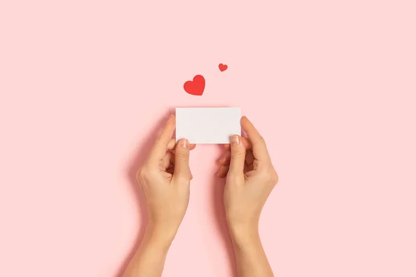 Manos de mujer sosteniendo tarjeta de San Valentín en blanco sobre mesa rosa — Foto de Stock
