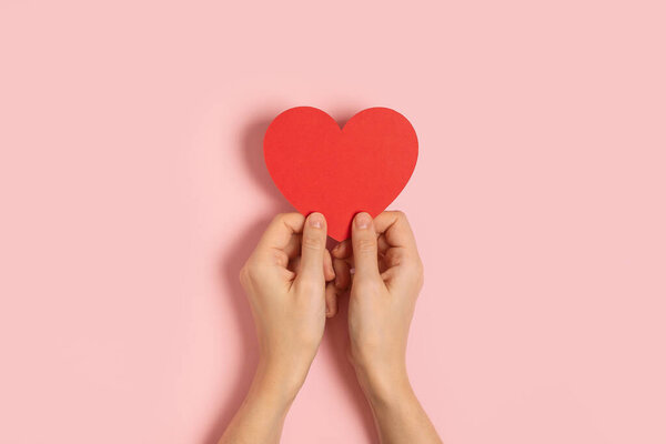 Woman hands holding blank Valentine card on pink table 