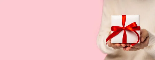 Kráska Žena ruce drží dárkové krabice s červenou mašlí na růžovém pozadí, zblízka. pastelové barvy, kopírovat prostor pro text. Valentýnský dárek. Banner for Christmas, hew year, birthday concept — Stock fotografie